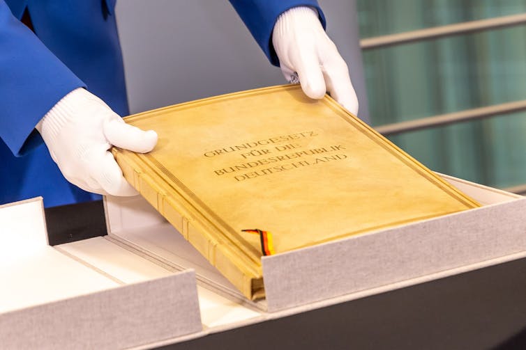 A person wearing white gloves holds up the original copy of the German constitution.