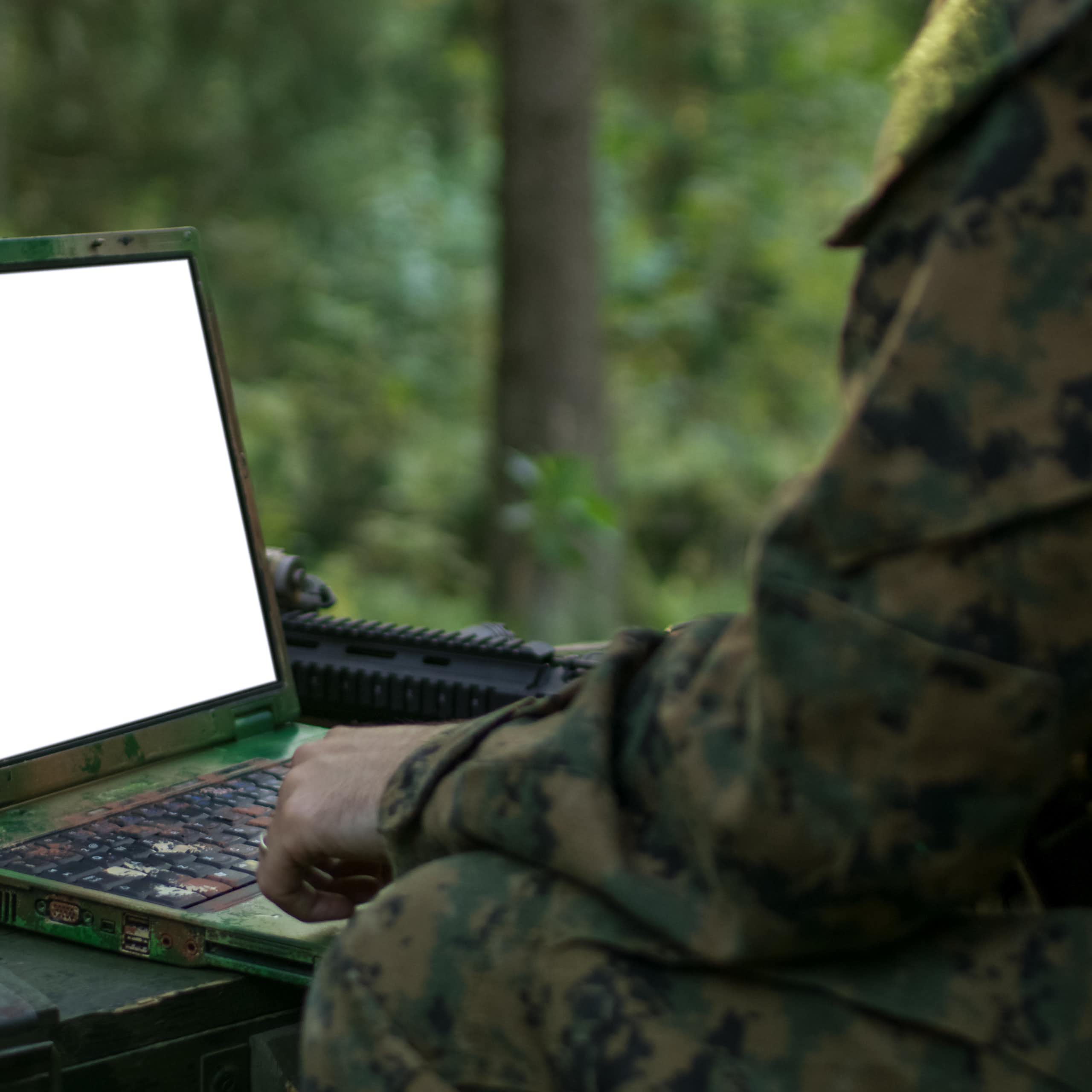 A person in camouflage clothing looks at a blank laptop screen.