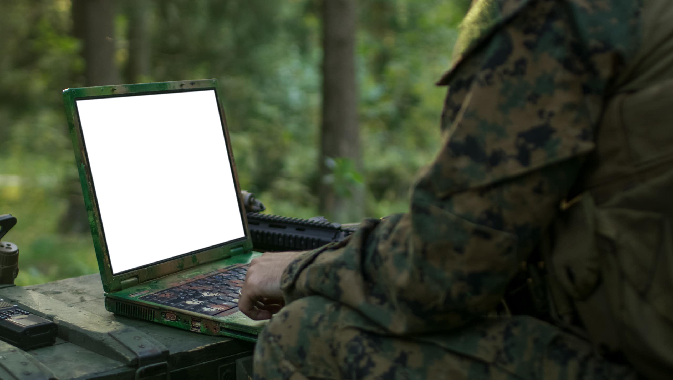 A person in camouflage clothing looks at a blank laptop screen.