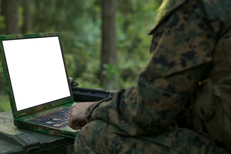 A person in camouflage clothing looks at a blank laptop screen.