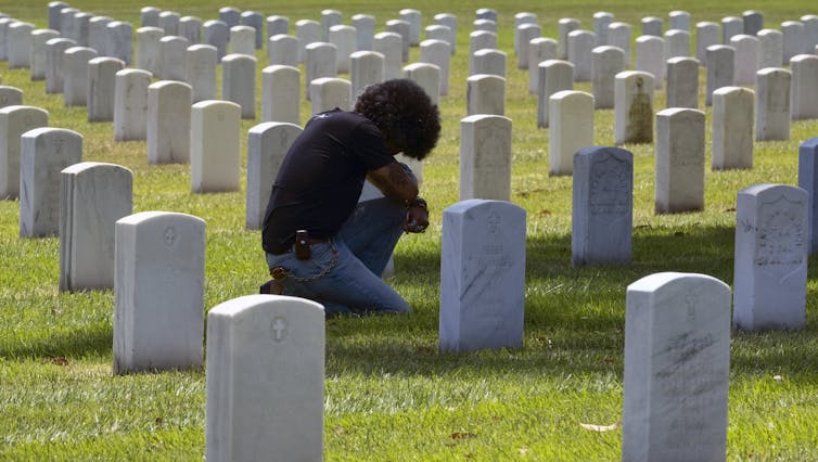 Person with bowed head on one knee at a grave among a row of graves