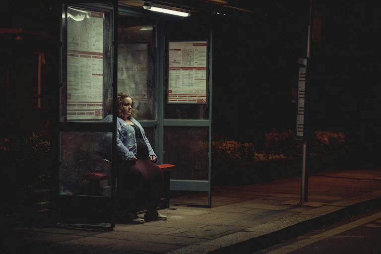 A woman sits alone at a bus stop at night