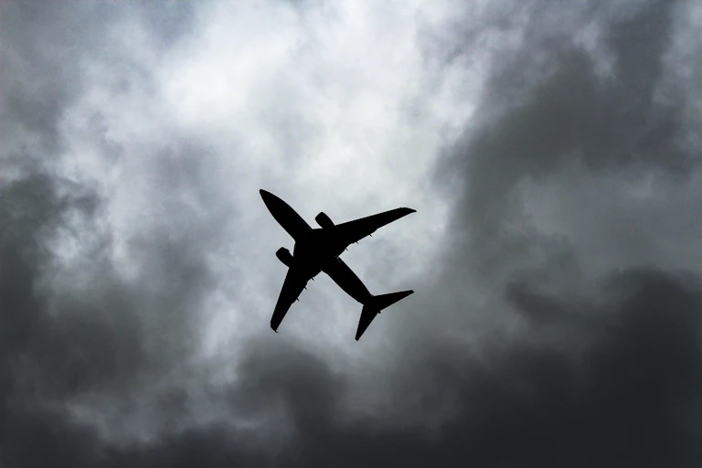 A silhouetted plane against a grey cloudy sky.