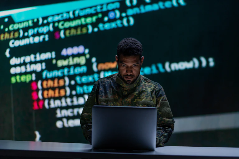 A hacker in military uniform stares at a laptop.