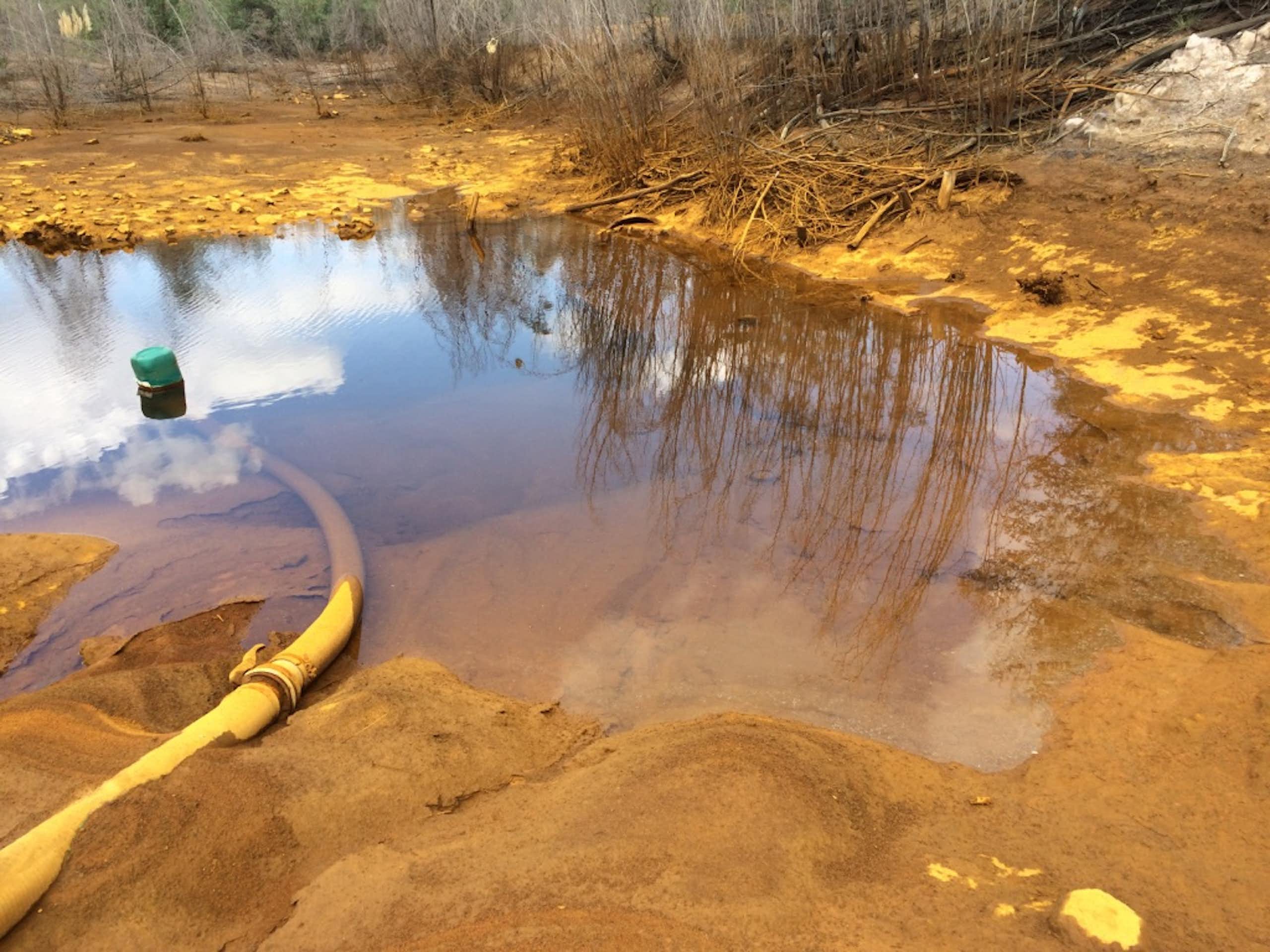 A yellow pipe feeds orange coloured water onto a large sandy area that looks very polluted
