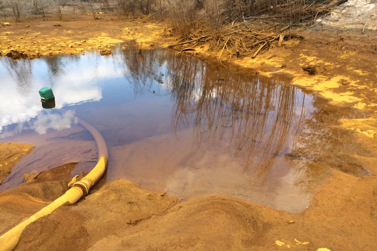 A yellow pipe feeds orange coloured water onto a large sandy area that looks very polluted