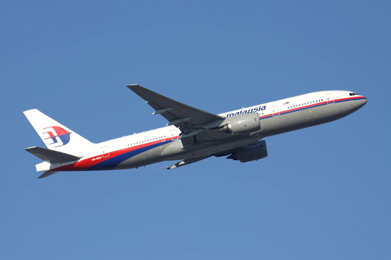 A Malaysian Airlines plane in flight against a blue sky.