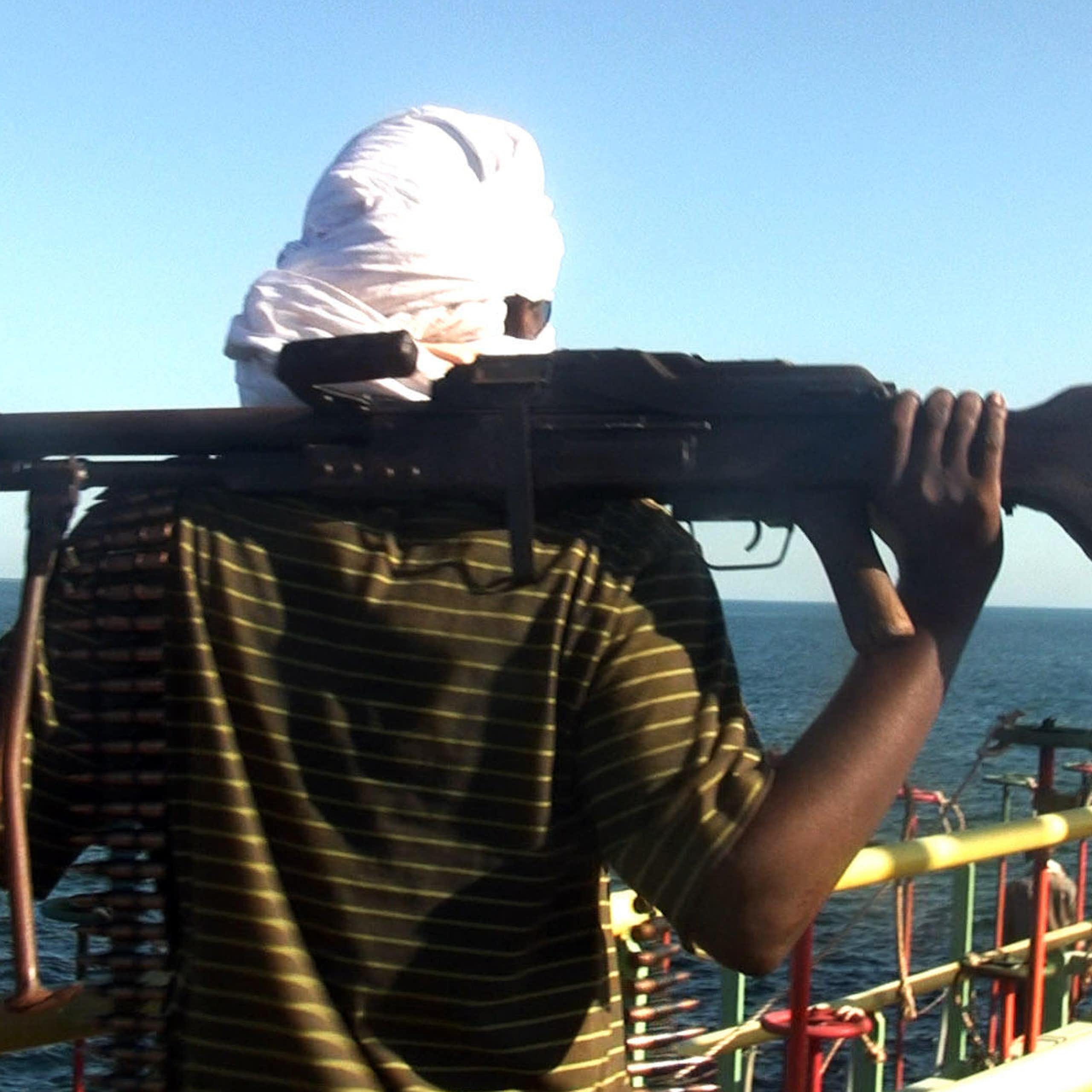 A man resting a large gun on his shoulders while looking out to sea from the deck of a boat.
