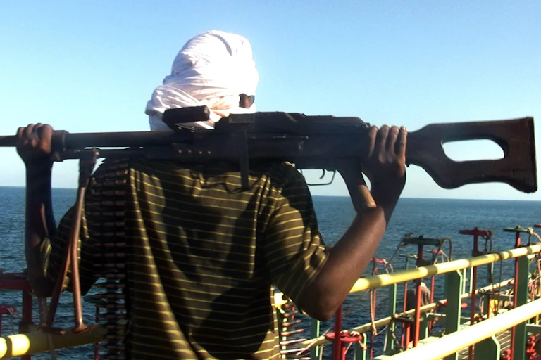 A man resting a large gun on his shoulders while looking out to sea from the deck of a boat.