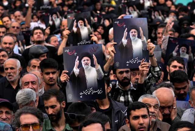 People hold up posters with pictures of a man in a black robe and turban with words below written in Persian.