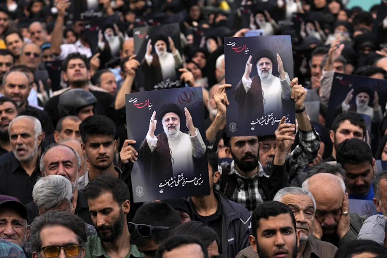People hold up posters with pictures of a man in a black robe and turban with words below written in Persian.