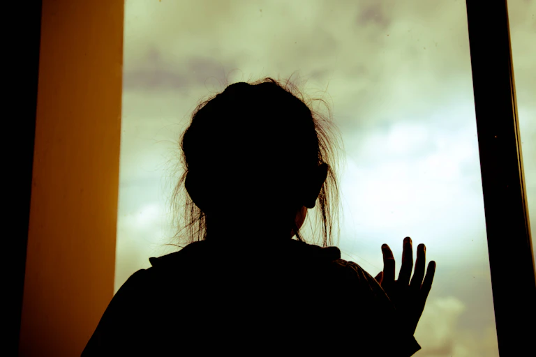 Silhouette sad little girl in room and looking out the window