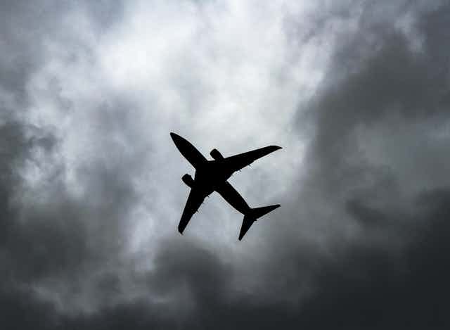 Um avião em silhueta contra um céu cinzento e nublado.
