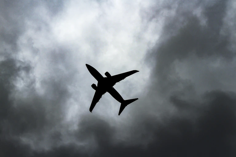 Um avião em silhueta contra um céu cinzento e nublado.