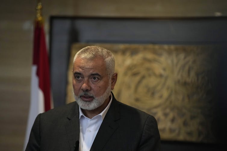 A man with thinning grey hair and a grey beard in a blue jacket and collared shirt.
