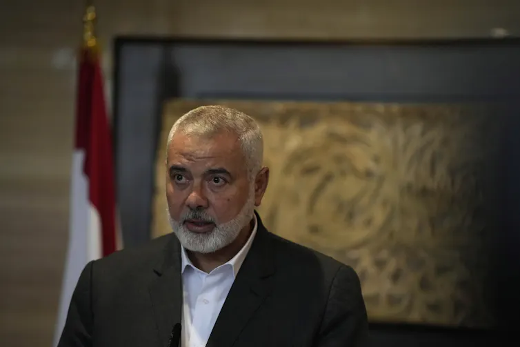 A man with thinning grey hair and a grey beard in a blue jacket and collared shirt.