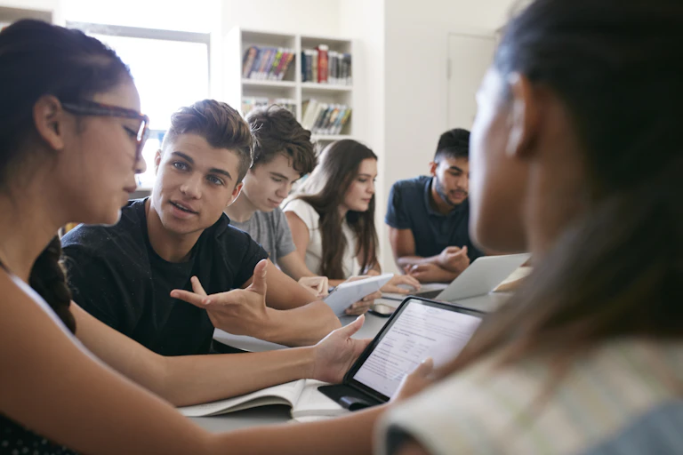 College students seated at a table talk and collaborate.