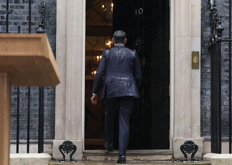 Rishi Sunak entrando na Downing Street com as costas encharcadas.