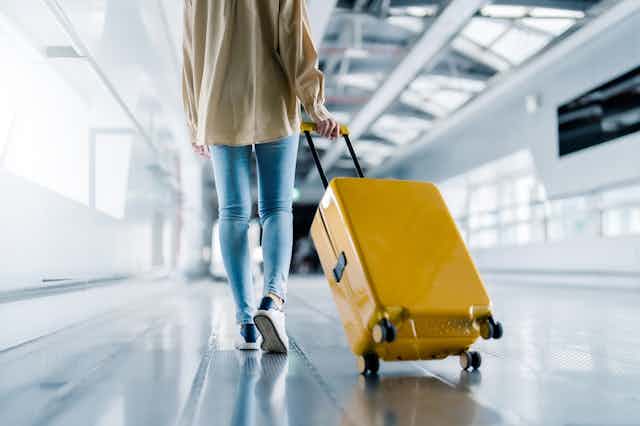 Woman in jeans pulling along yellow suitcase at airport