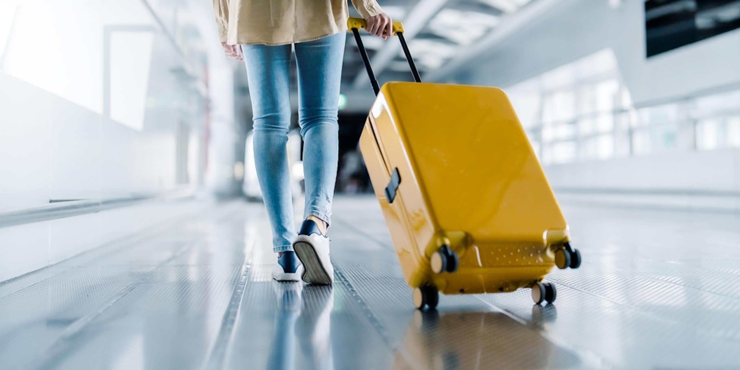 Woman in jeans pulling along yellow suitcase at airport