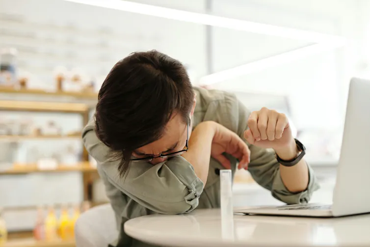 A man sneezes into his elbow at work.