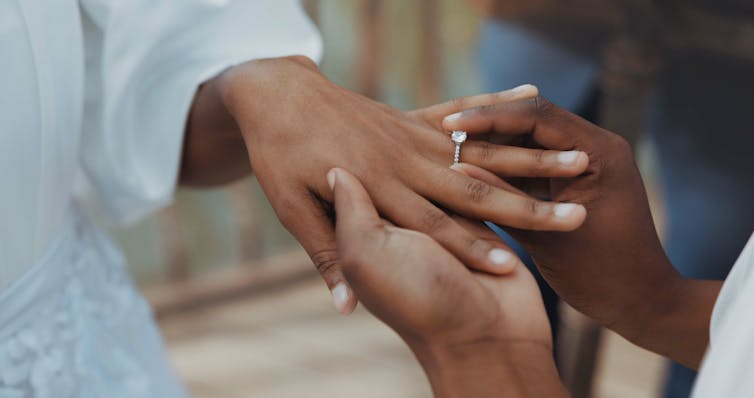 closeup of two hands, one puts wedding ring on the other