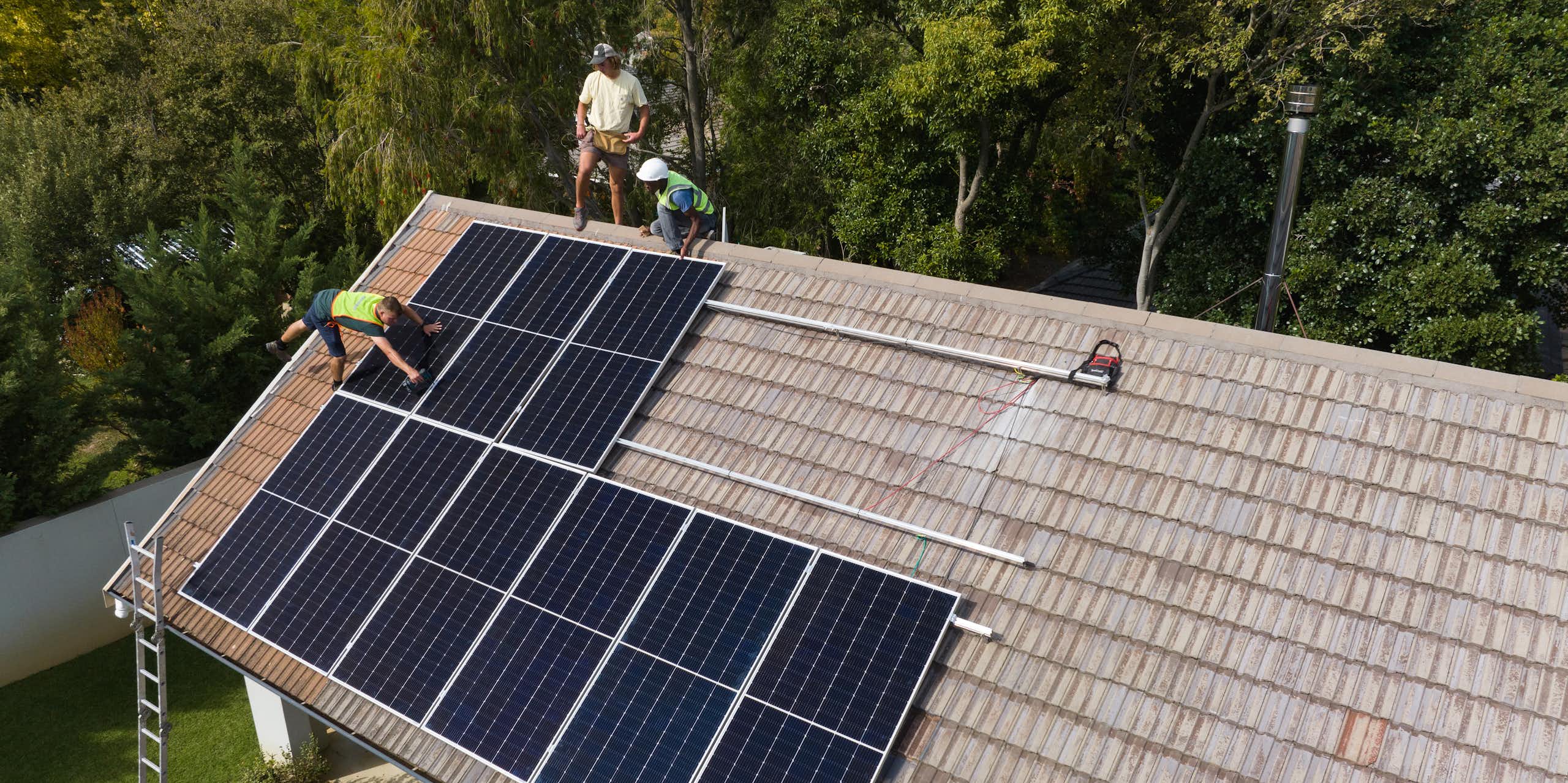 Three men on a roof are fitting solar panels