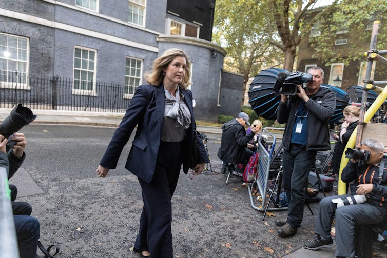 Penny Mordaunt entrando na Downing Street, enquanto fotógrafos de cada lado dela tiram fotos
