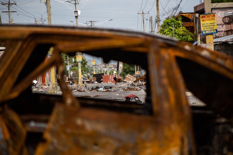 A wrecked street shot through the window of a burned-out car.