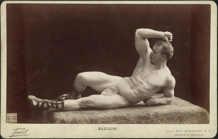 A muscular man rests on one arm, naked but for a fig leaf in a vintage photograph.