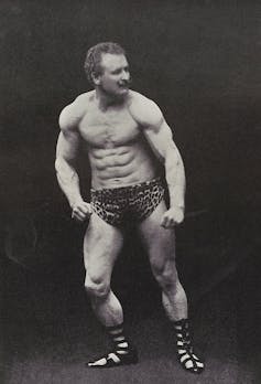 A muscular man poses in animal print shorts in a vintage photograph.