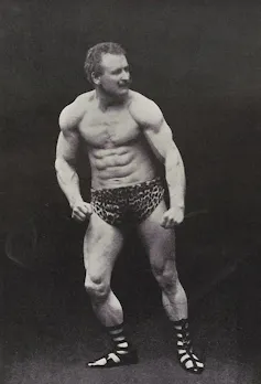A muscular man poses in animal print shorts in a vintage photograph.