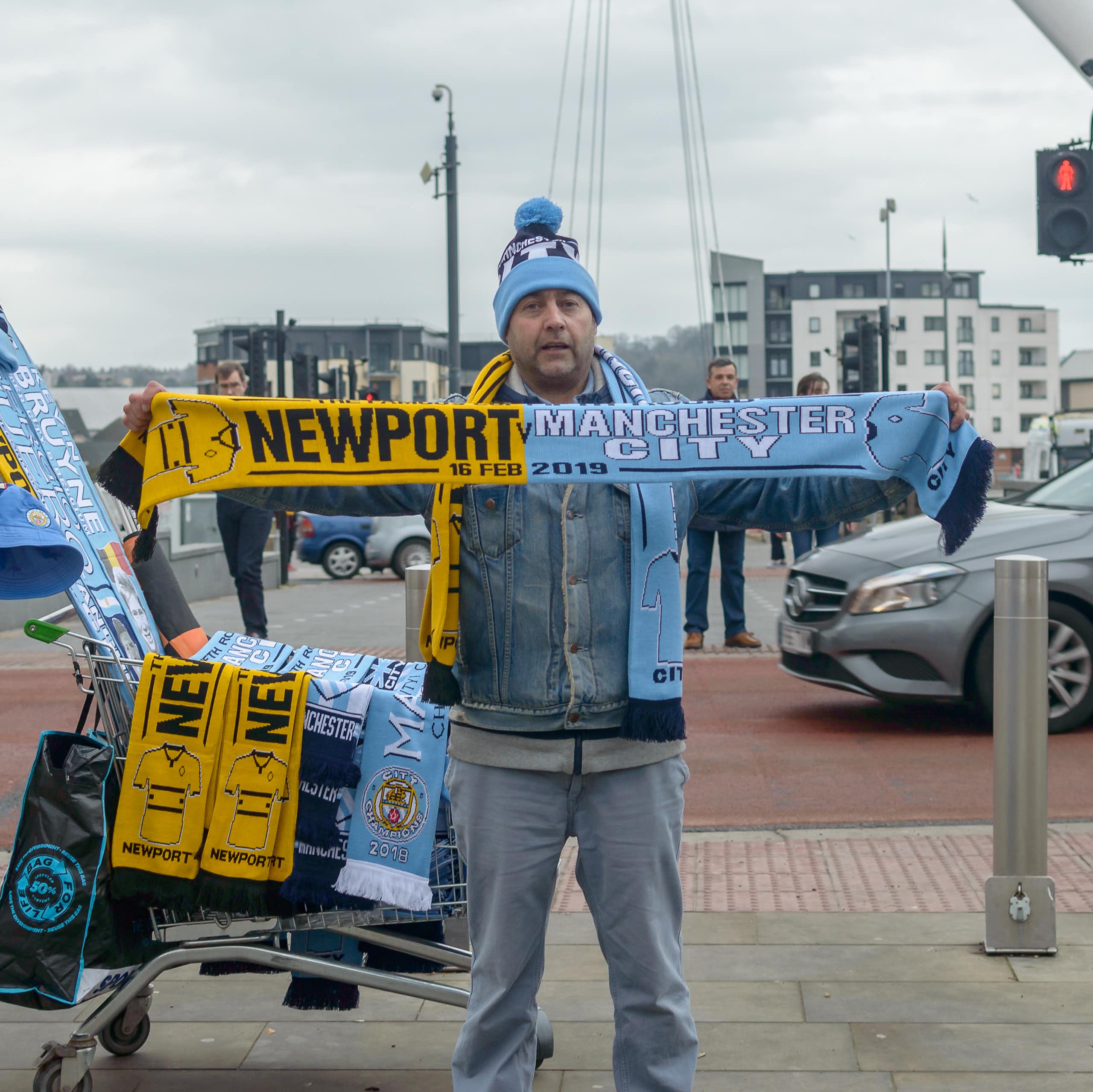 Man holding football scarf with the names and colours of Newport County and Manchester City.