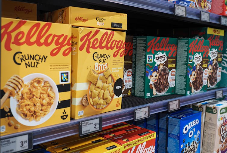 A row of colorful Kellogg's cereal boxes stands on a supermarket shelf.