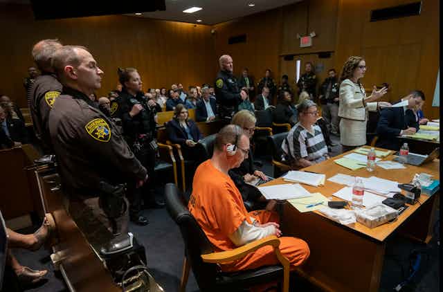 Man in orange jumpsuit awaits sentencing.