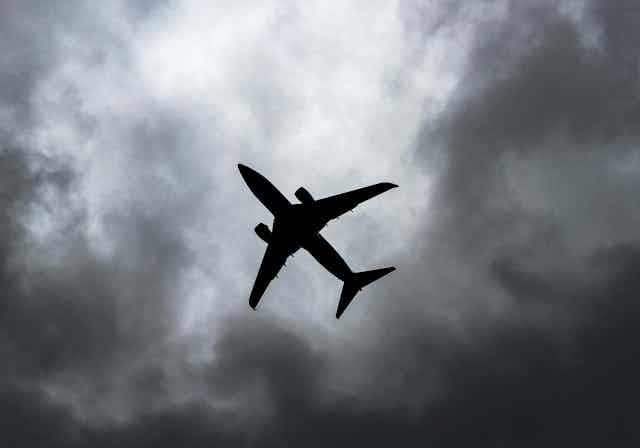 Silhouette d'un avion dans un ciel gris et nuageux.
