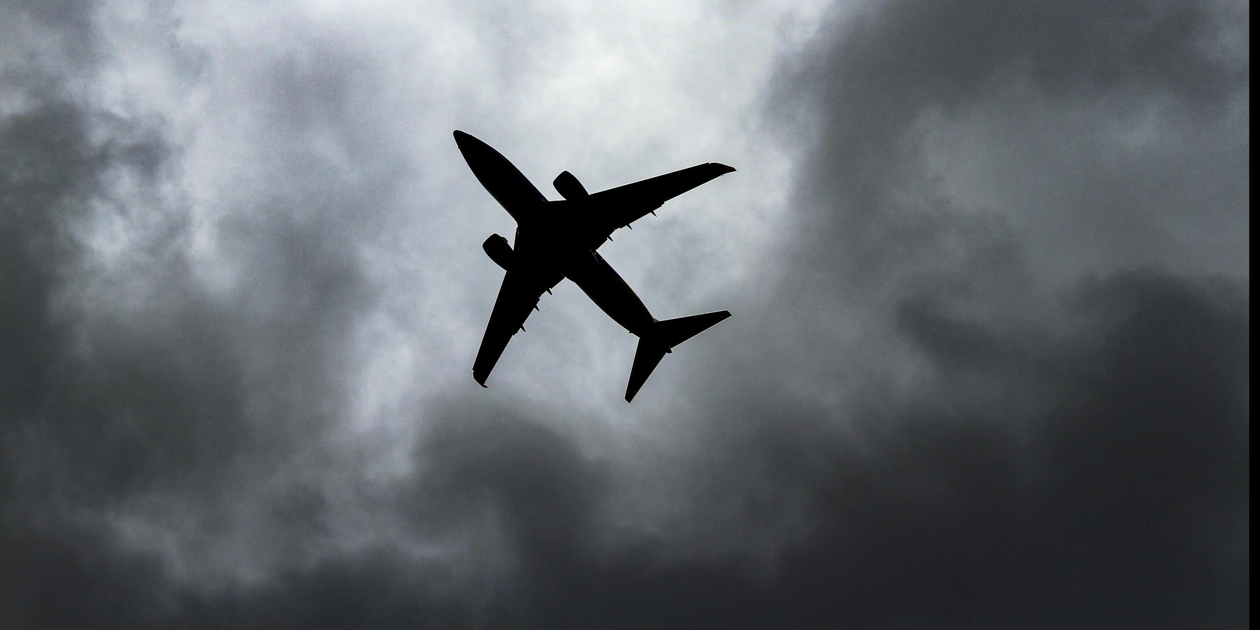 Silhouette d'un avion dans un ciel gris et nuageux.