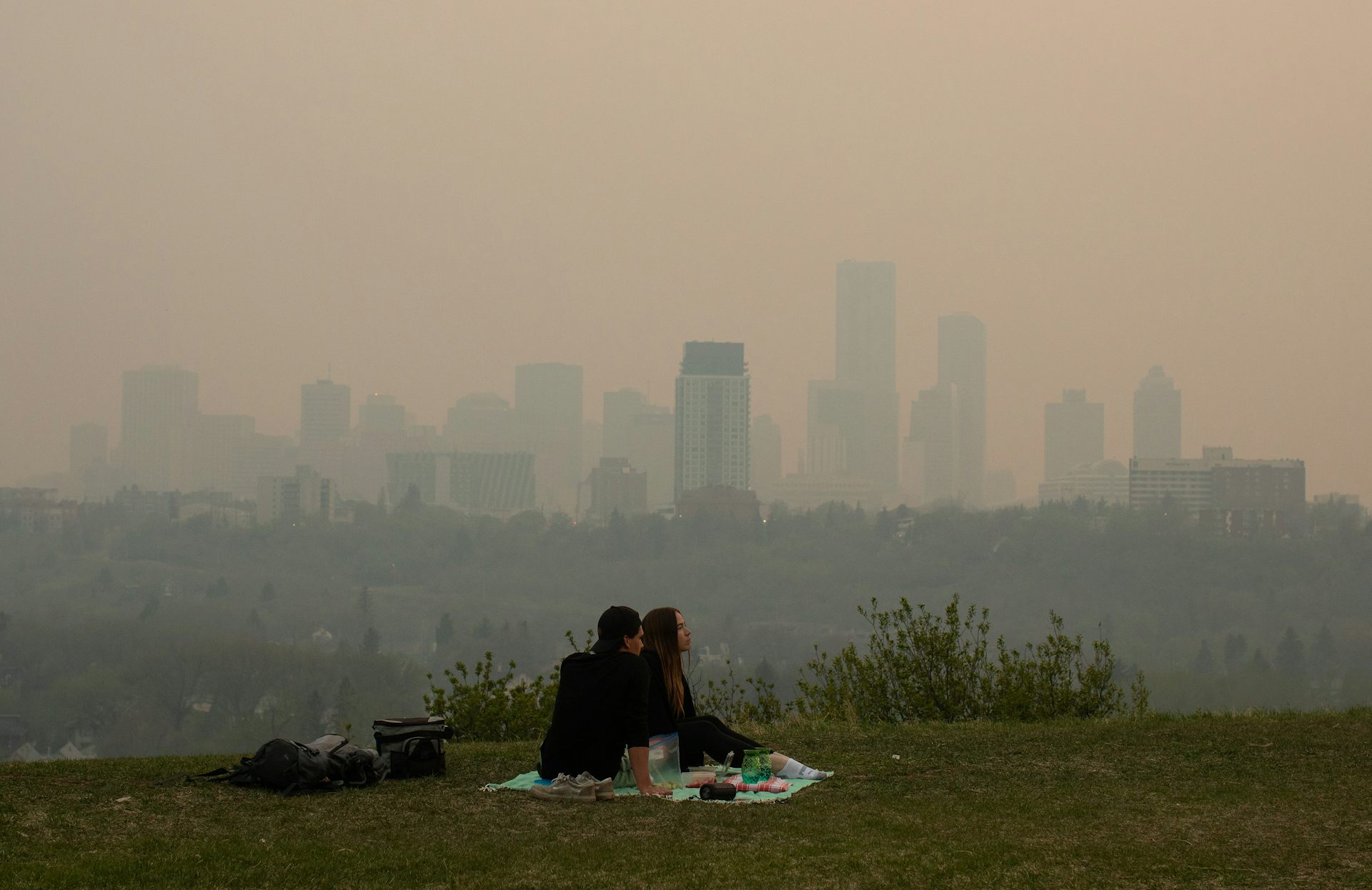A couple sit on a grassy field under a smoky sky