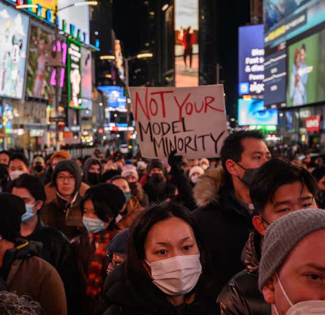A person holds a "Not Your Model Minority" sign amid a large crowd in New York City's Times Square on Jan. 18, 2022.