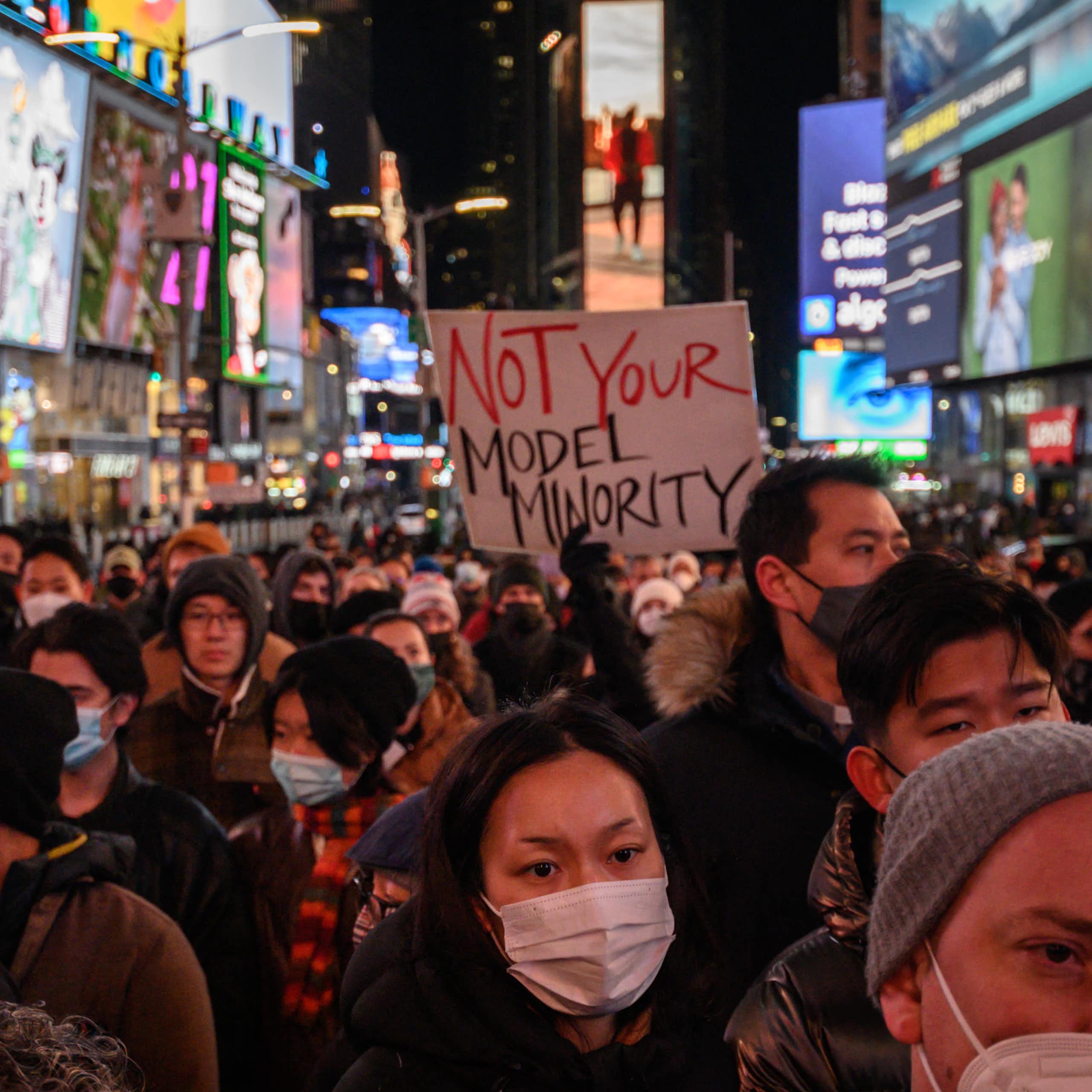 A person holds a "Not Your Model Minority" sign amid a large crowd in New York City's Times Square on Jan. 18, 2022.