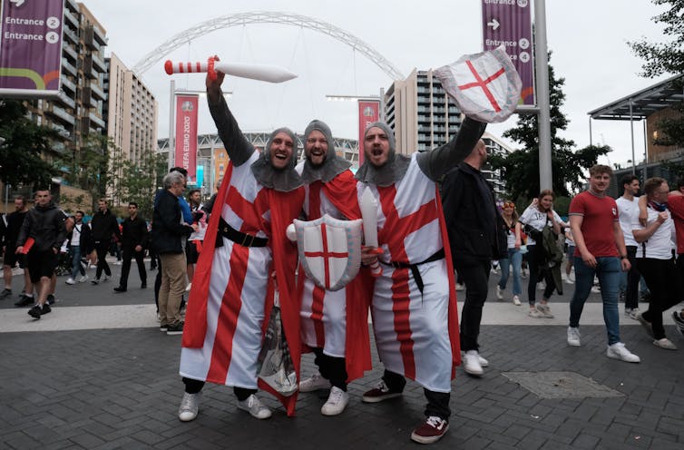 Three men dressed as knights, draped in the England flag.
