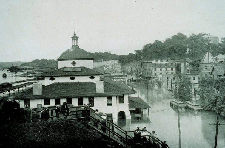 A view of downtown over the railroad depot with roads filled with water and the river bridge visible in the distance.