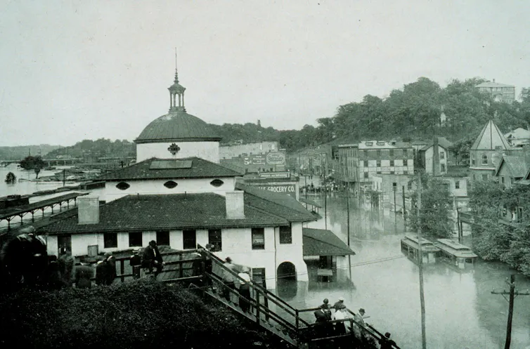 A view of downtown over the railroad depot with roads filled with water and the river bridge visible in the distance.
