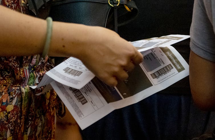 Close up of a woman's hand holding a printed out ticket with barcodes and the word 'ticketmaster' on it.