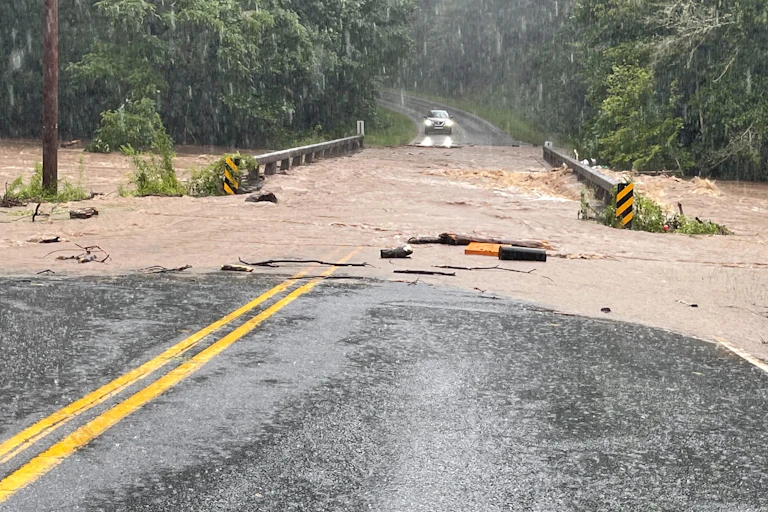 . Vehicles in murky water and a washed-out bridge with shops behind.