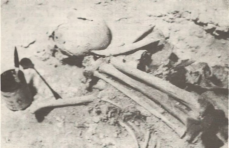 A grayscale sepia image showing a collection of human bones partially embedded in the ground.