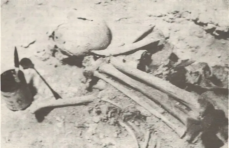 A grayscale sepia image showing a collection of human bones partially embedded in the ground.
