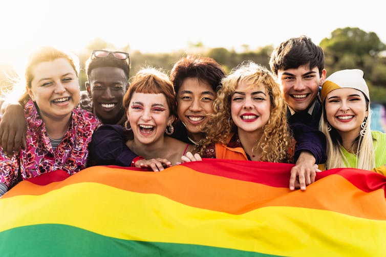 A group of young people of diverse races holding a rainbow flag.