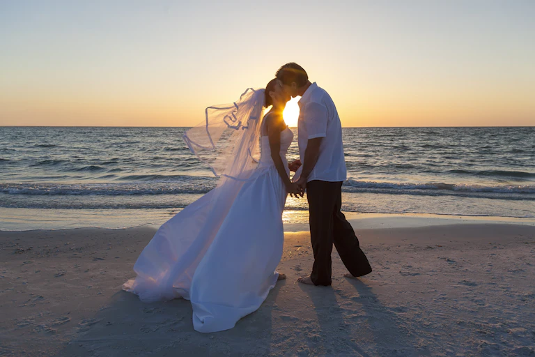 bride and groom kissing on beach at sunset