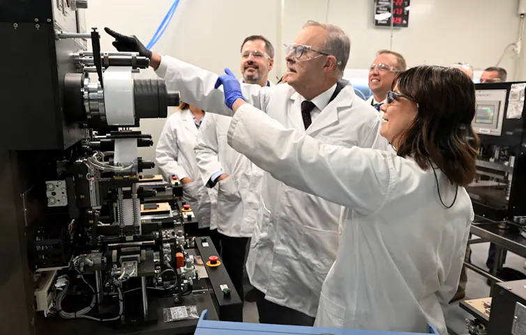 A group of people wearing white lab coats pointing to shiny things an industrial lab including Science Minister Ed Husic and Prime Minister Anthony Albanese during a visit to the Queensland University of Technology Advanced Battery Facility in Brisbane,